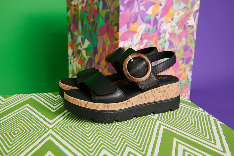Cammie black sandals against a green background