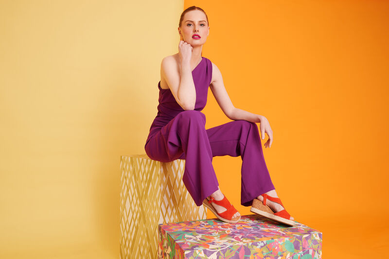 Woman in a purple jumpsuit wears orange wedge sandals