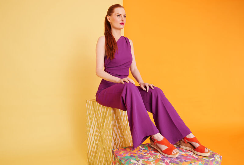 woman wears purple jumpsuit and orange wedge sandals