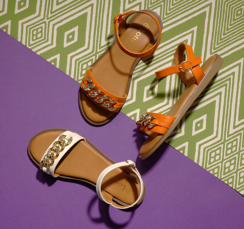 Neeta sandals - orange and white against a purple and green background