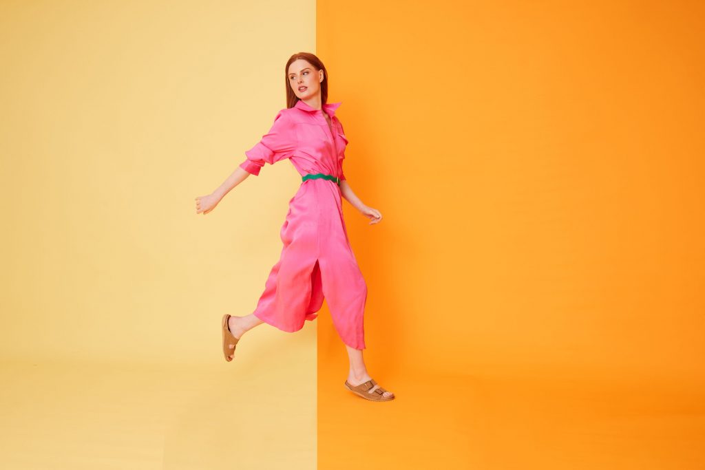 woman in a pick dress and muted flats runs across an orange background